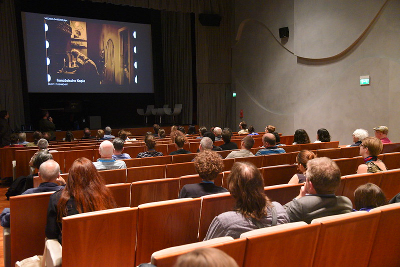 Image of theatre during a collegium session. Public is facing a screen.